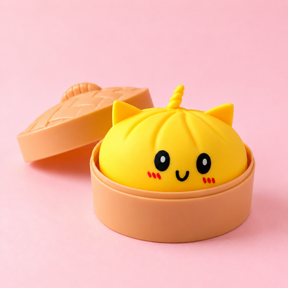Squishy bao kawaii jaune avec oreilles de chat et corne de licorne dans son panier vapeur, fond rose